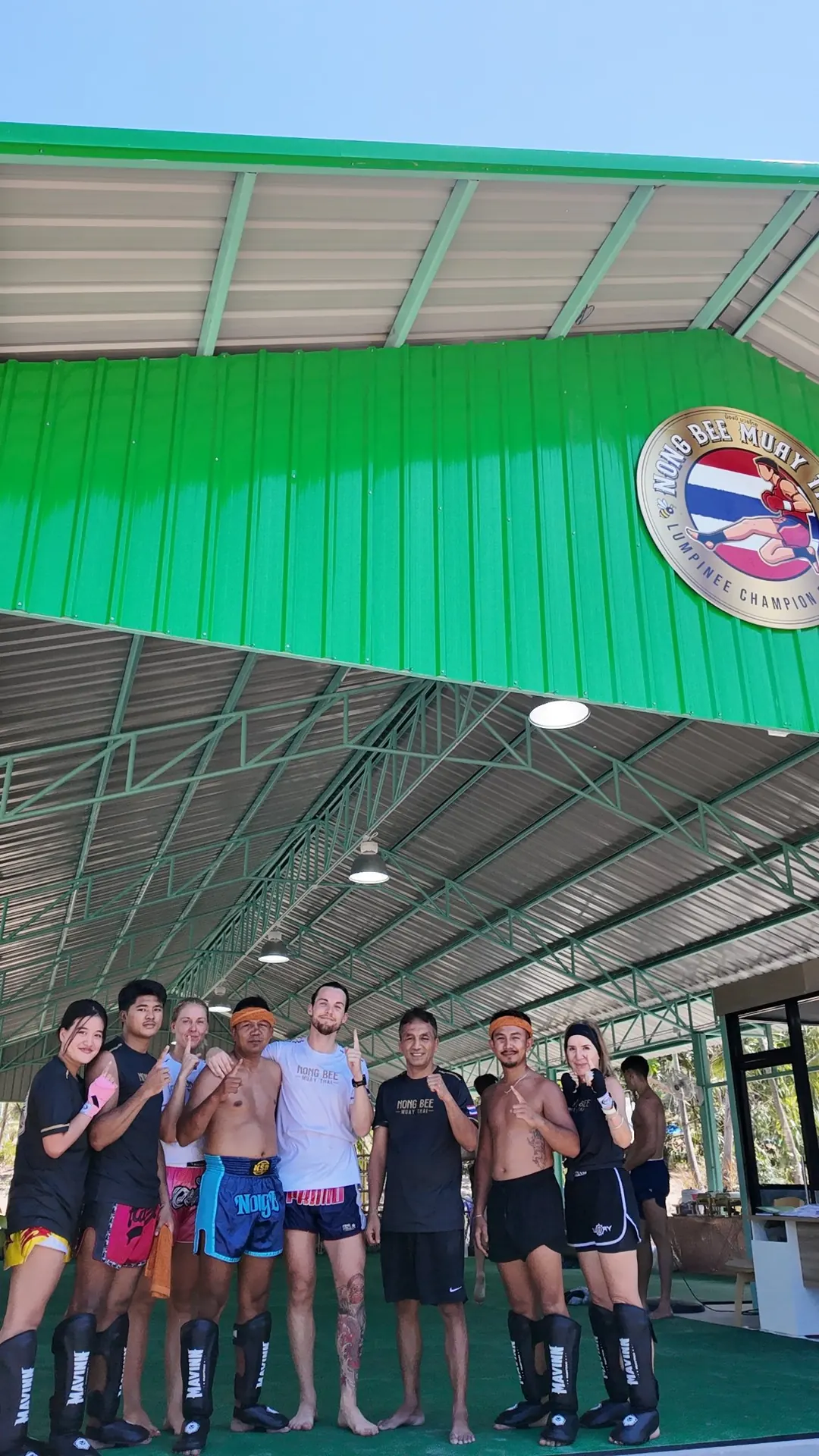 Trainers and clients posing under the Nong Bee Muay Thai gym sign